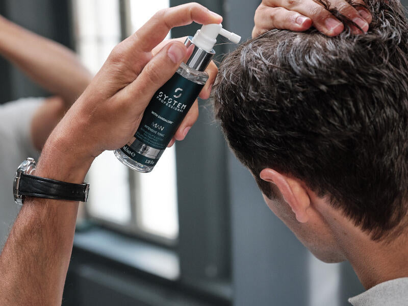 Mann mit kurzen dunklen Haaren sprüht sich das Intensiv Tonic aus der System Professional MAN Serie in das Haar.
